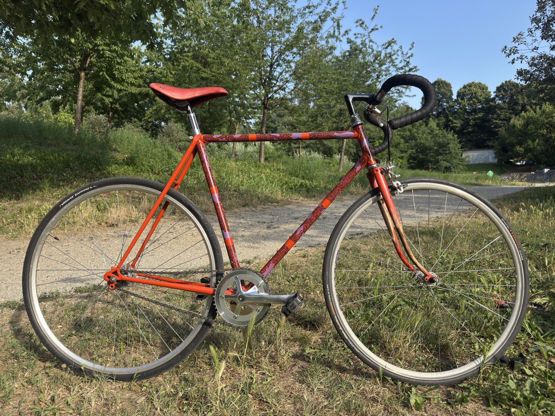 Full side view of the orange hand-painted road bicycle in a park